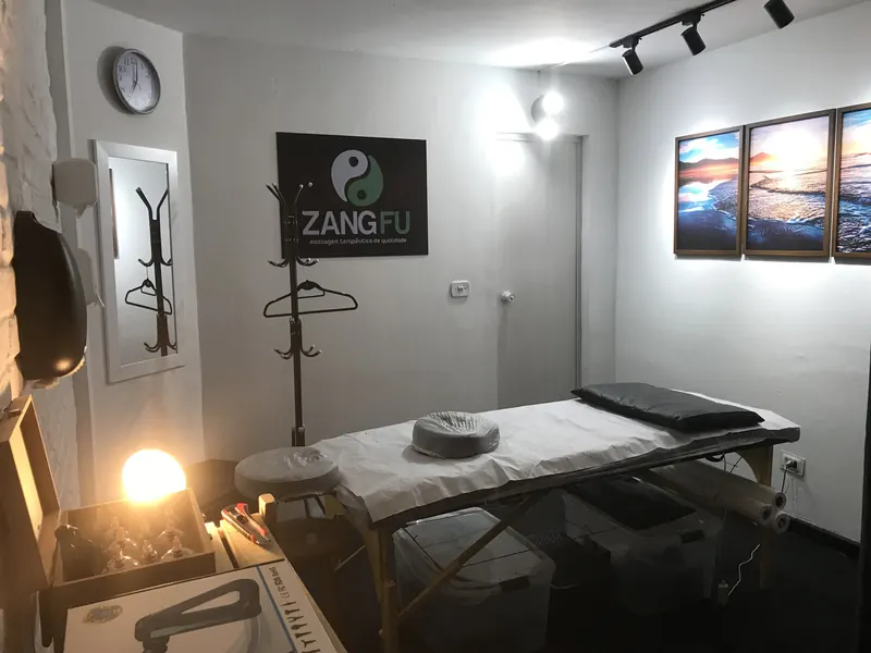 Sala de massoterapia da Zang Fu Consolação com maca, iluminação suave e quadros na parede