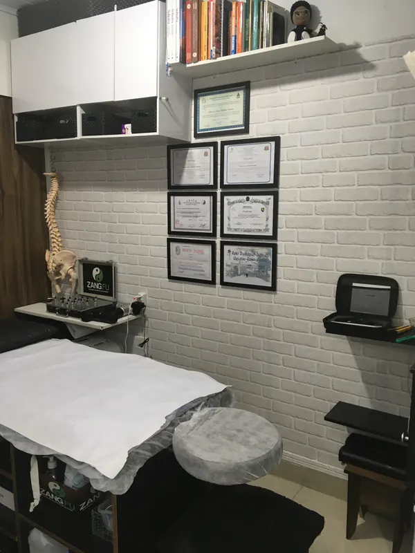 Sala de massagem da Zang Fu Pinheiros com maca e certificados dos terapeutas na parede
