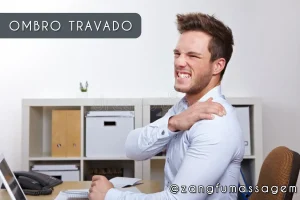 Homem no escritório fazendo careta de dor e segurando o ombro travado